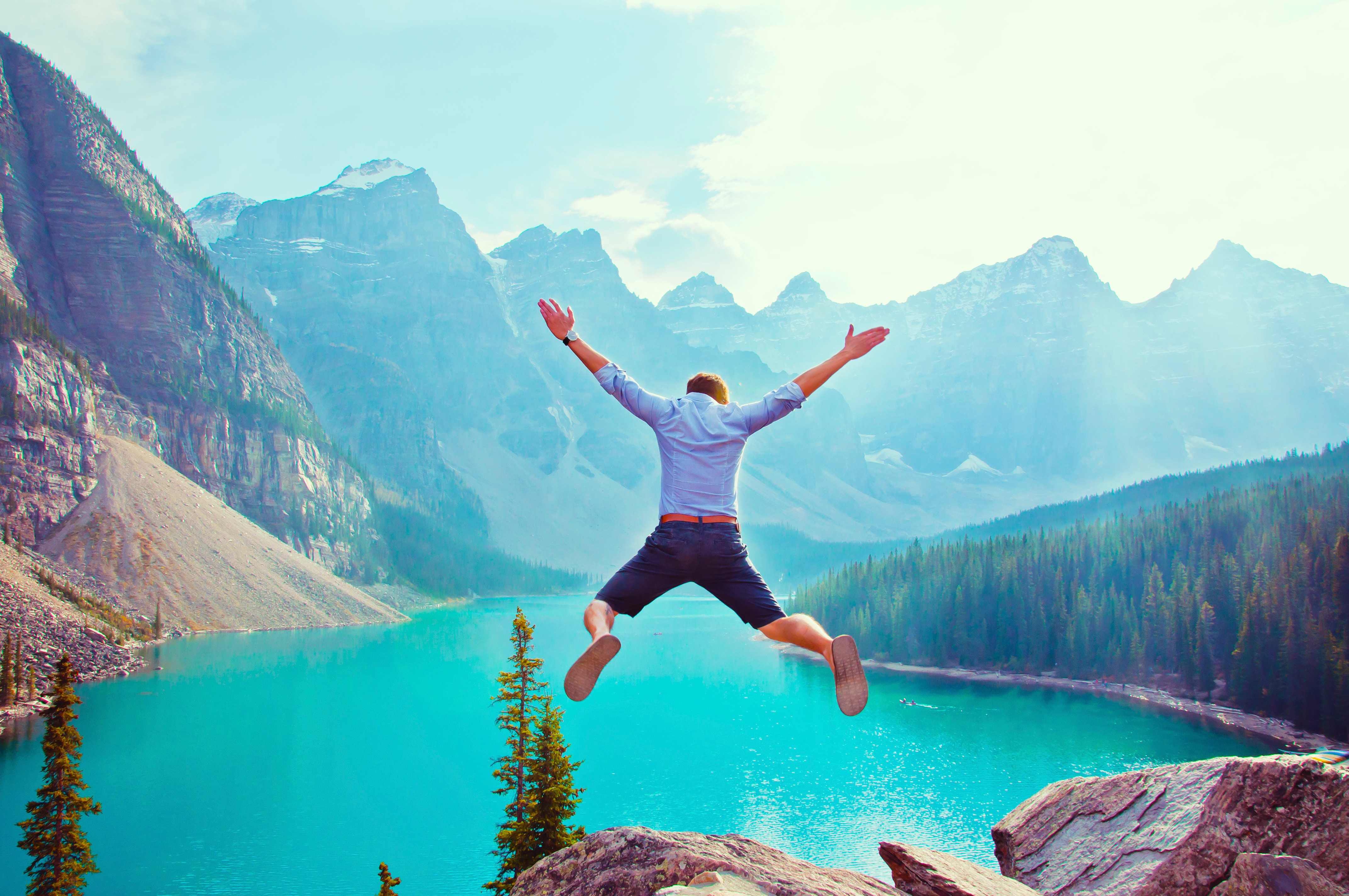 man jumping in front of a lake surrounded by tall mountains