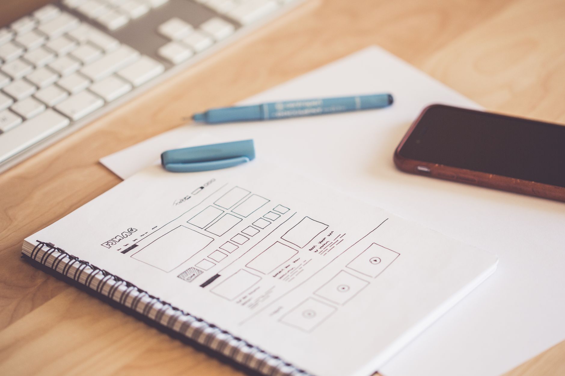 Website wireframe sketches beside a smartphone and keyboard