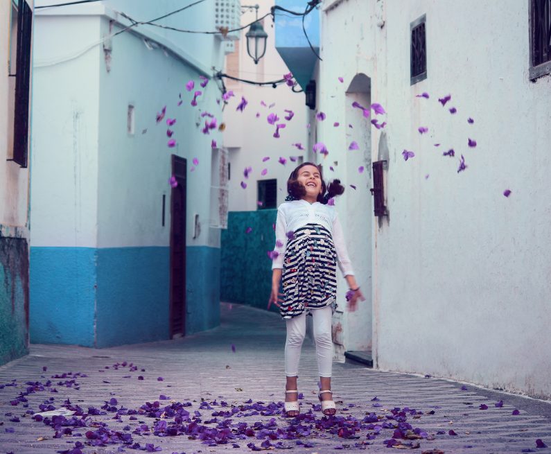 young girl standing in an alley amongst falling flower petals