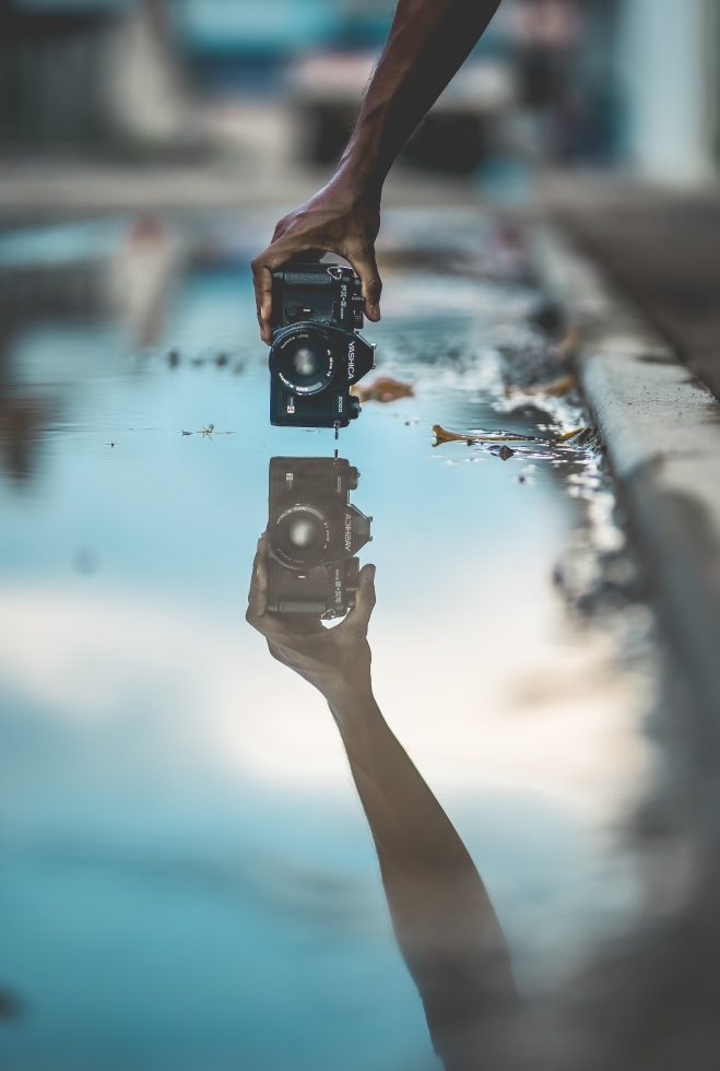person holding a camera above a flooded gutter